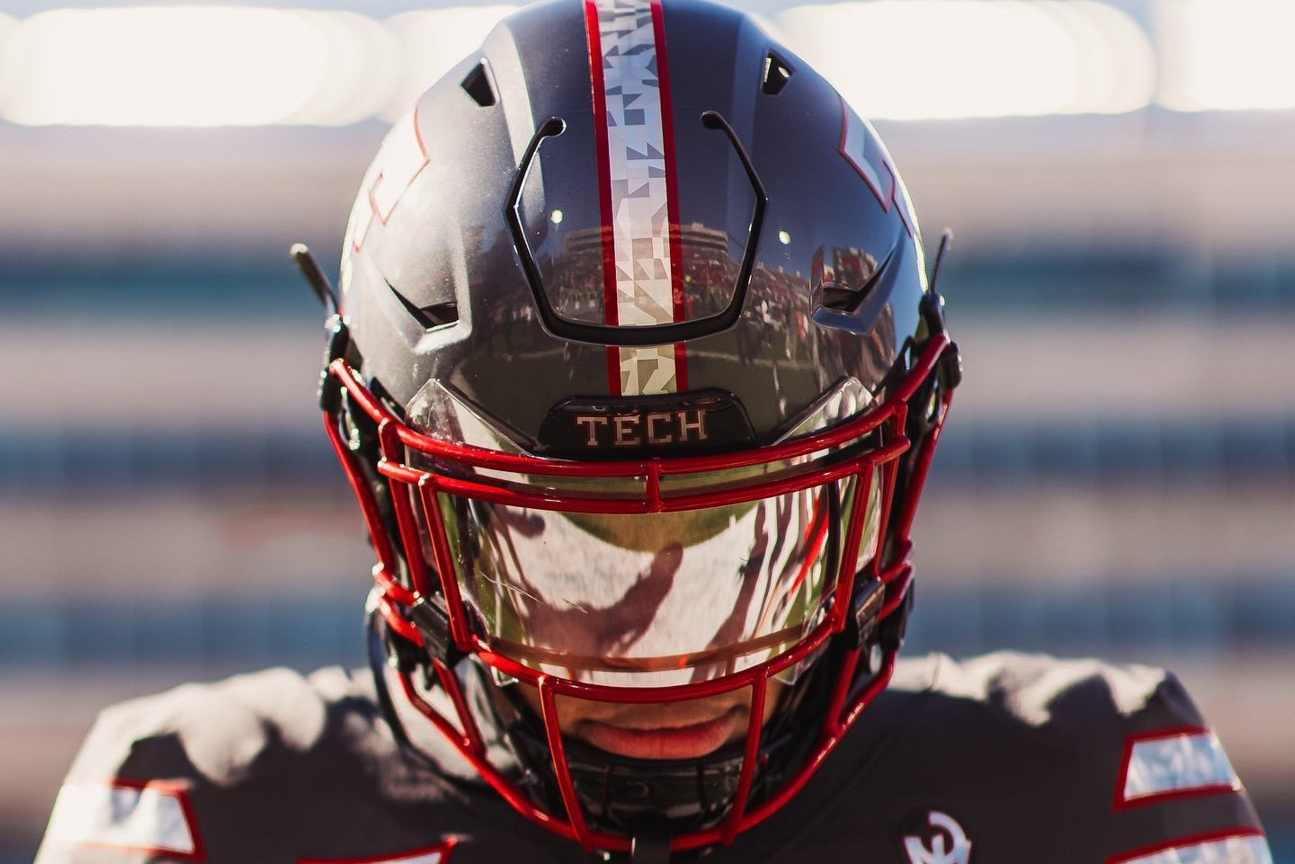 Person wearing a football helmet and jersey with 'TECH' branding on a blurred stadium background